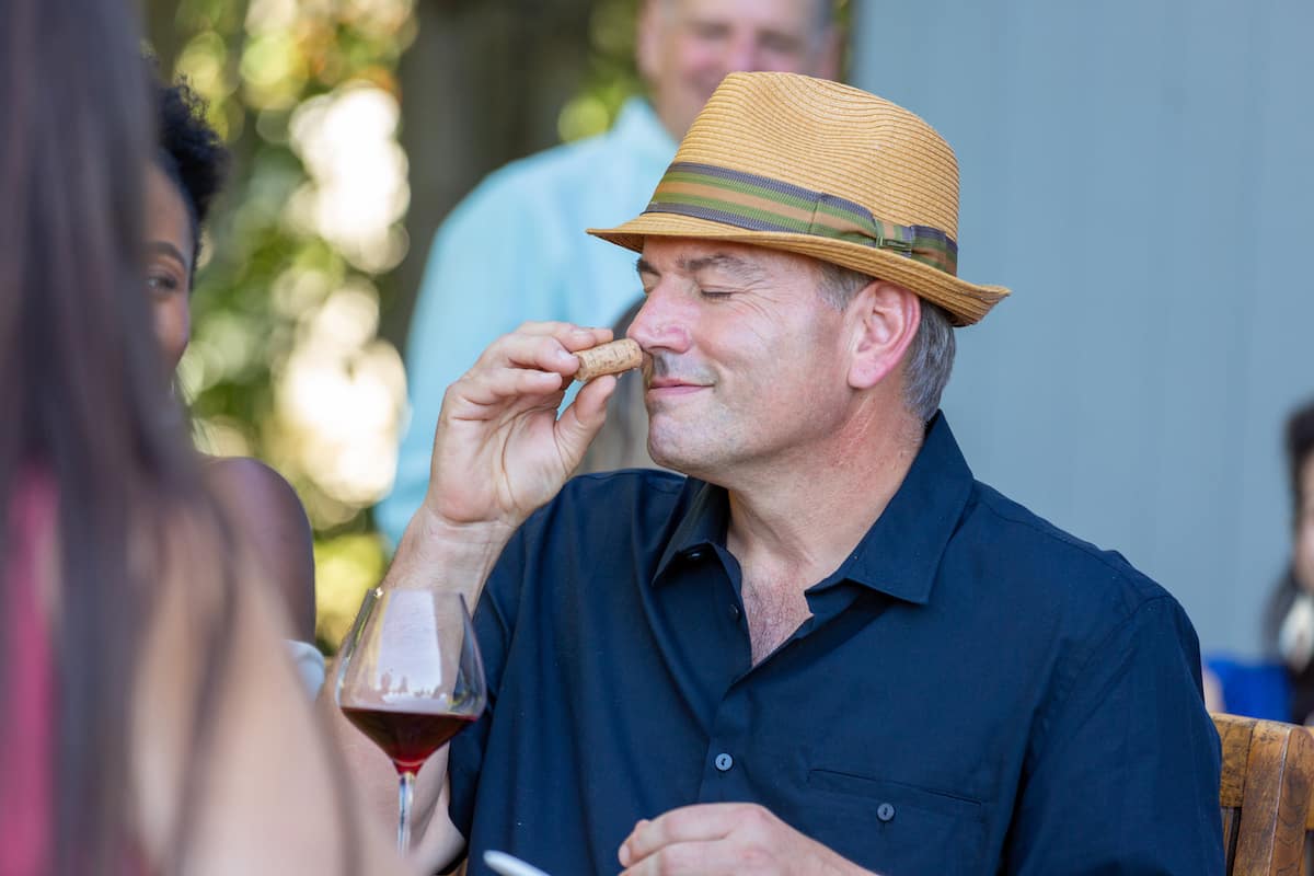 At the wine tasting event held at the Sebastopol winery vineyard estate, a male wine enthusiast is seen smelling the cork of a bottle of Sonoma Coast Pinot Noir.